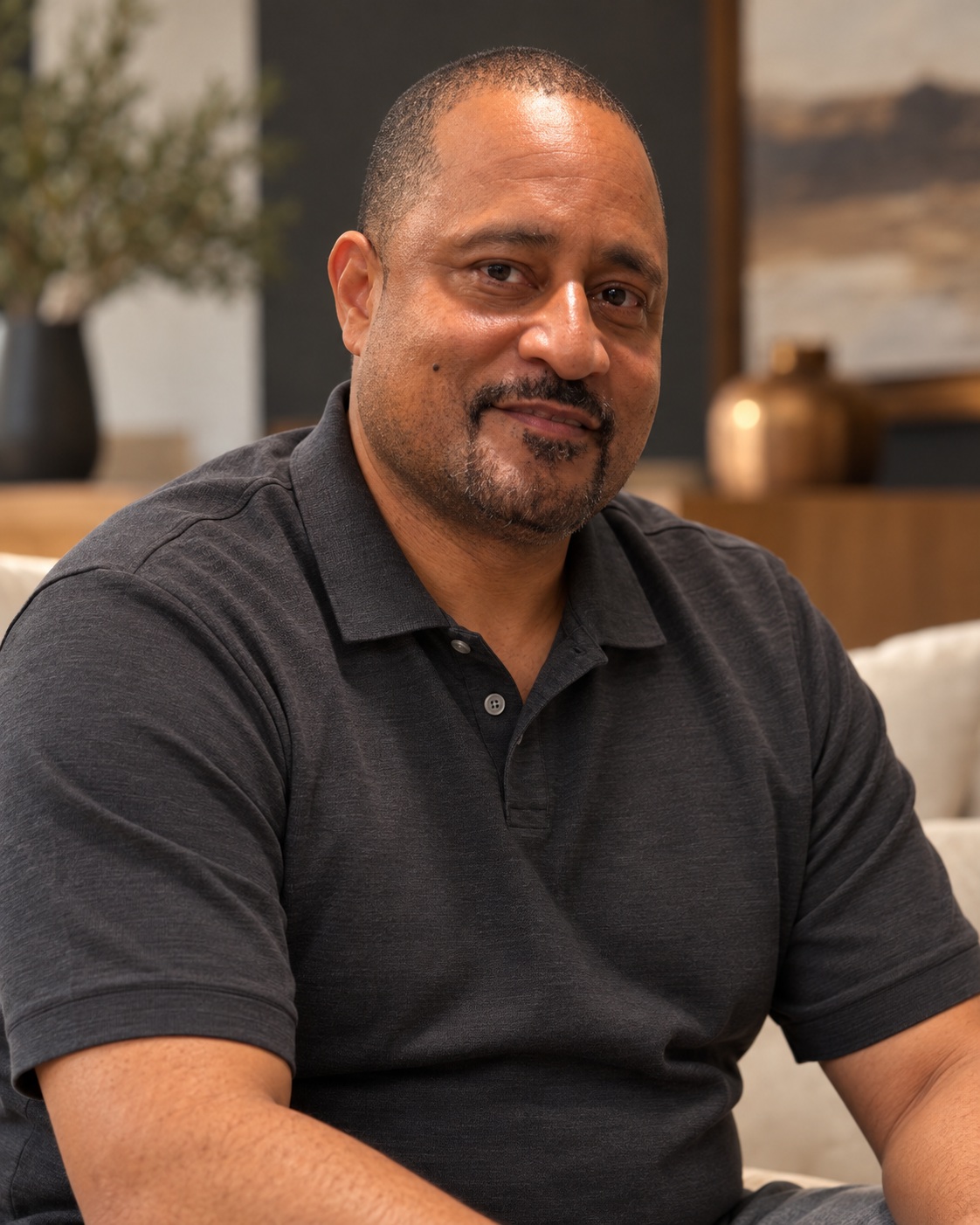 Kiyam Dade in a charcoal polo, smiling in a warmly lit interior